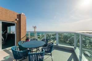 Un balcon doté d’une balustrade en verre, une table avec des chaises et une vue sur la ville et l’océan.