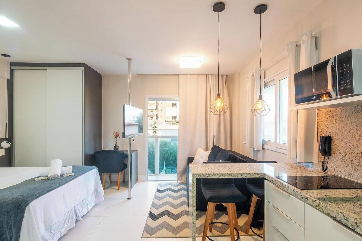 A compact hotel room with a bed, a small desk, a kitchenette, and a view of the outside.