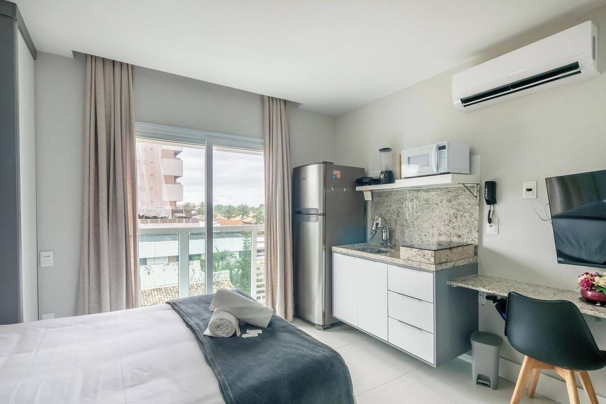 A hotel room with a bed, kitchenette, and a balcony with a view.