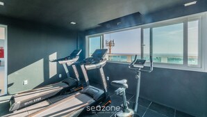 Une salle de sport équipée de tapis de course et d’un appareil elliptique, dotée de grandes fenêtres et offrant une vue sur la ville.