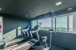 Une salle de sport équipée de tapis de course et d’un appareil elliptique, dotée de grandes fenêtres et offrant une vue sur la ville.