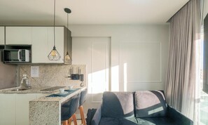 A modern kitchen with a microwave, two pendant lights, and a granite countertop. - Sua estadia com conforto em prédio c/ piscina e a Praia a Poucos Passos - PSPs (Salvador)