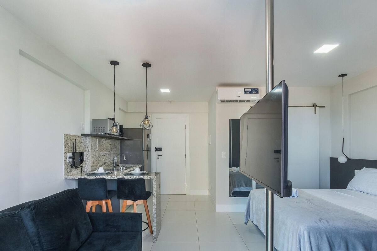 A compact hotel room with a bed, a TV, a kitchenette, and a seating area.
