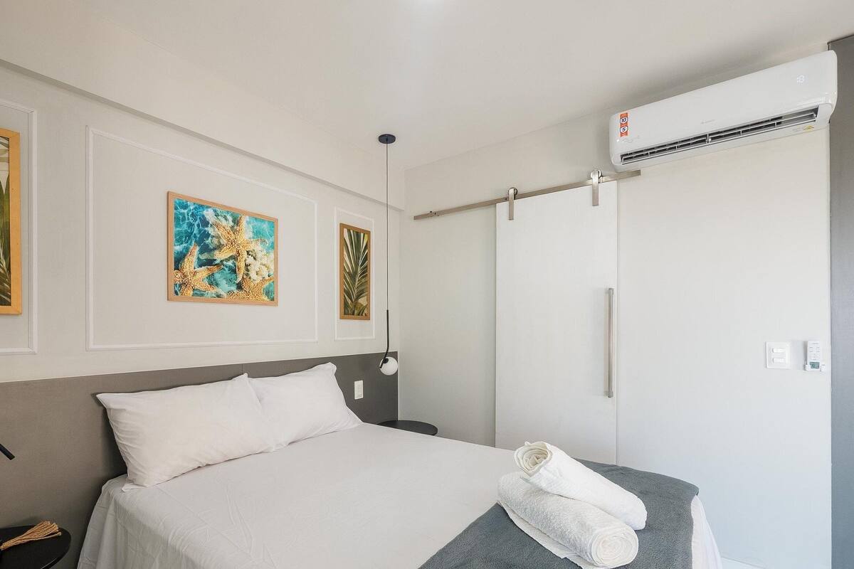 A hotel room with a bed, a wall-mounted air conditioner, and two framed pictures.