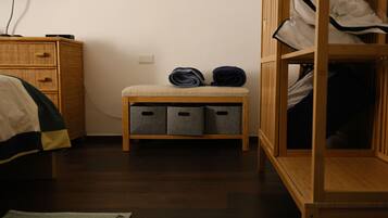 A bedroom with a wooden wardrobe, a bedside table with storage bins, a bed with a striped blanket, and a wall socket.