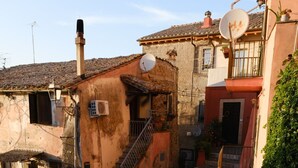 Una stretta via acciottolata, fiancheggiata da edifici antichi con architettura tradizionale, tra cui una scala che conduce a un ingresso al secondo piano.