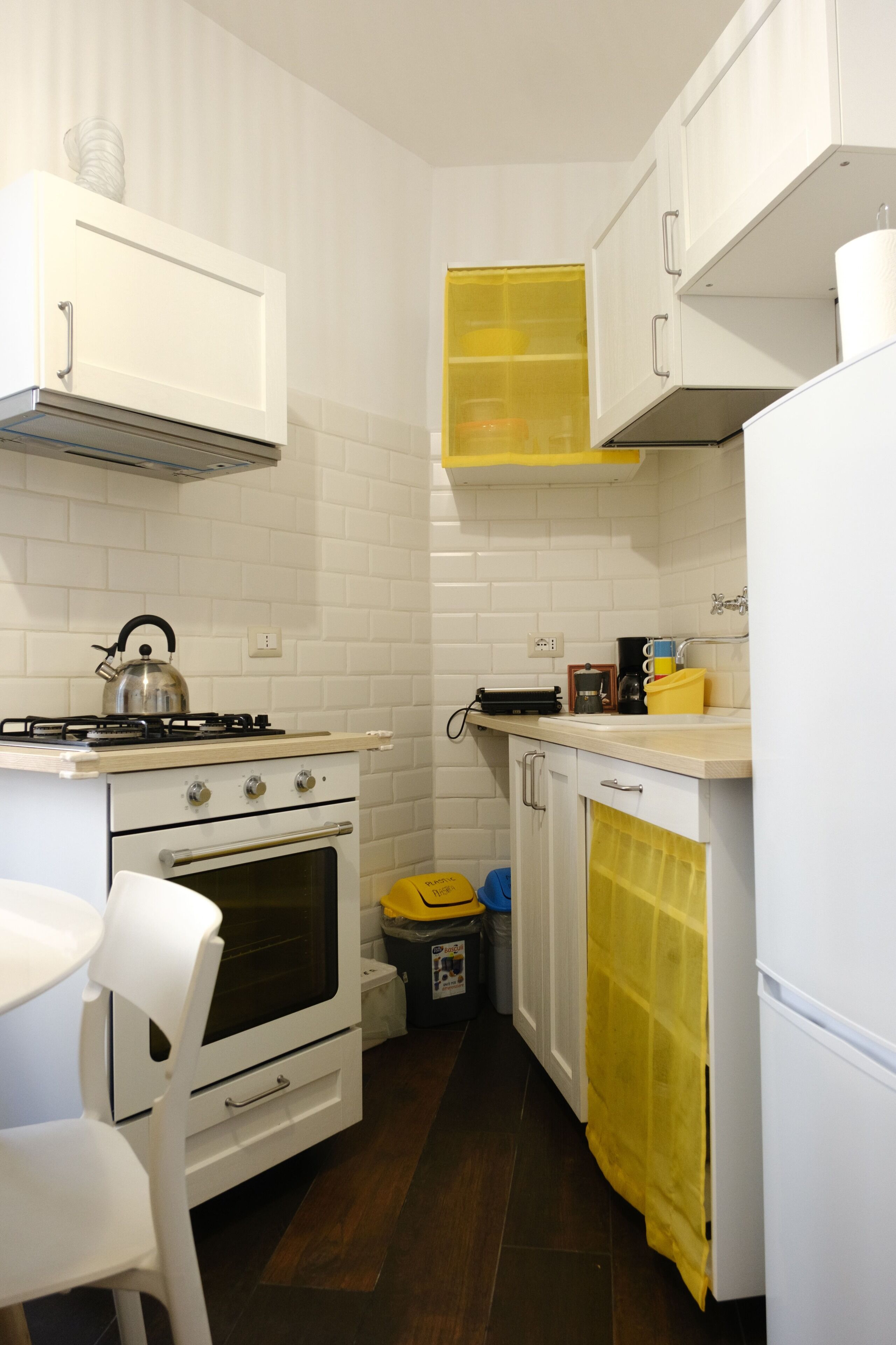 Une cuisine de taille réduite avec des meubles blancs, une cuisinière à gaz, un four et un rideau jaune.