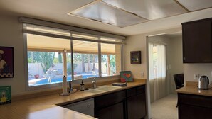A kitchen with a large window, a sink, a dishwasher, and a countertop with a kettle. - Charming 3-bedroom house with AC in sunny Scottsdale (Scottsdale)