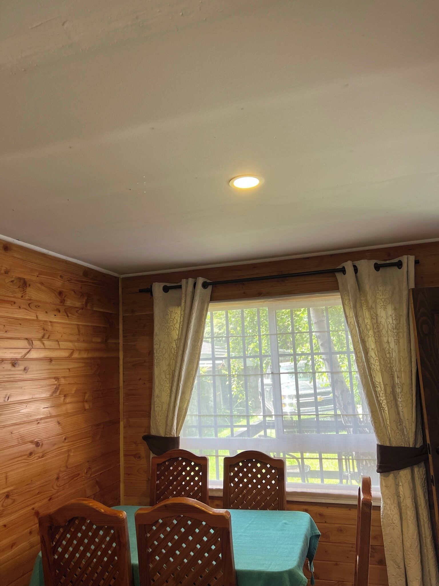 A wooden-paneled room with a table and chairs, a window with curtains, and a ceiling light.