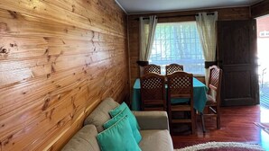Tunnelmallinen huone, jossa on puuseinä, turkoosinsinisillä koristetyynyillä varustettu sohva, ruokapöytä tuoleineen ja näkymä ikkunasta.