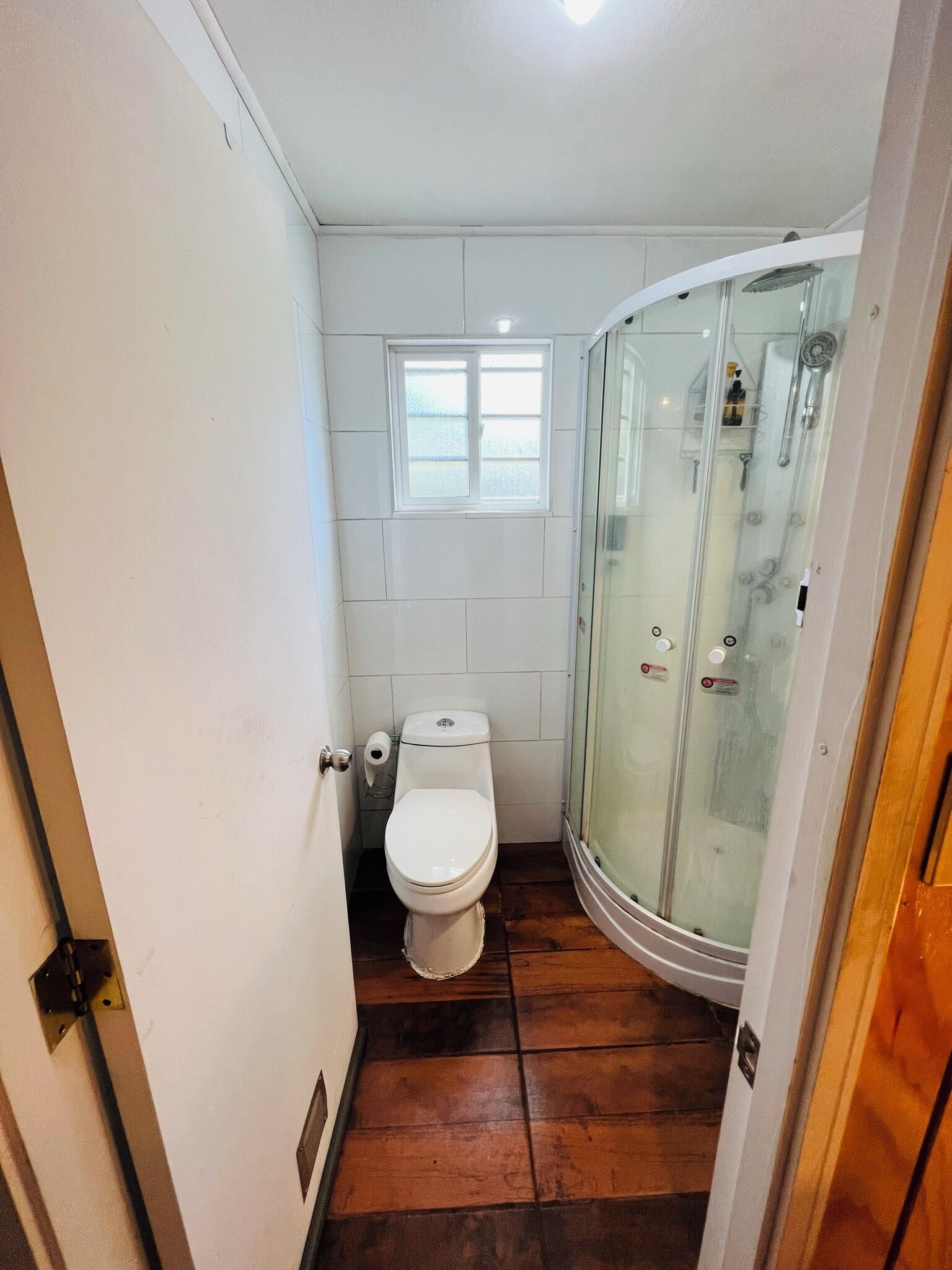 A small bathroom with a toilet, a window, and a glass-enclosed shower.