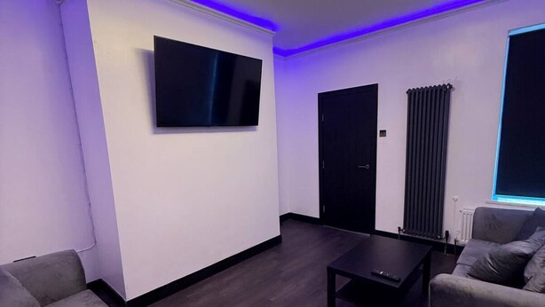 Ein modernes Wohnzimmer mit einem an der Wand befestigten Flachbildfernseher, einem dunklen Holzboden und zwei grauen Sofas.
