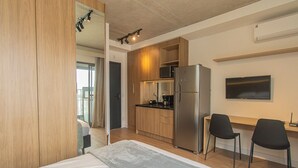 Et moderne hotelværelse med seng, tekøkken, TV og skrivebord med stole.