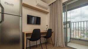 Et moderne hotelværelse med et træskrivebord, to sorte stole, et fladskærms-tv og et stort vindue med udsigt over byen.