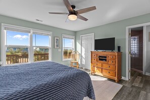 Une chambre dotée d’un grand lit, d’un ventilateur de plafond, d’une commode, d’un téléviseur et d’une porte donnant sur un balcon.