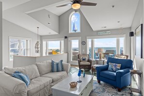 A spacious living room with a high ceiling, large windows, and a view of the ocean. - Ocean Views! New 4bd Home, very close to Beach! (Oak Island)