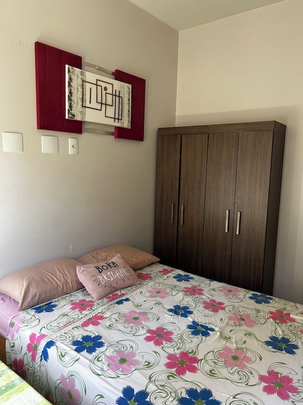 A bedroom with a bed, a wardrobe, a wall-mounted artwork, and a red shelf.