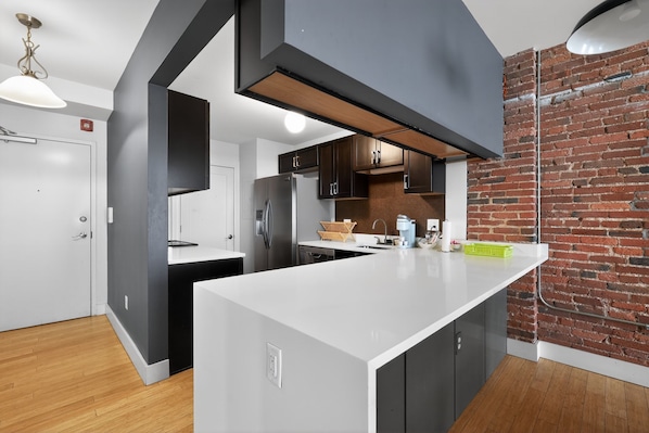 A modern kitchen with a white countertop, dark cabinetry, and a brick wall.