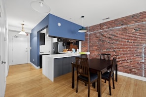 A modern kitchen with a blue accent wall, a dining area with wooden chairs, and a brick wall.