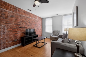 A living room with a brick wall, a television, a sofa, a chair, and a table.