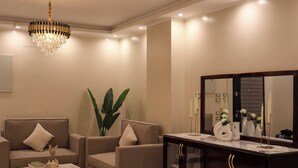 Una sala de estar moderna con un juego de sofá, una mesa de centro, una planta grande, un mueble de madera oscura y una araña.