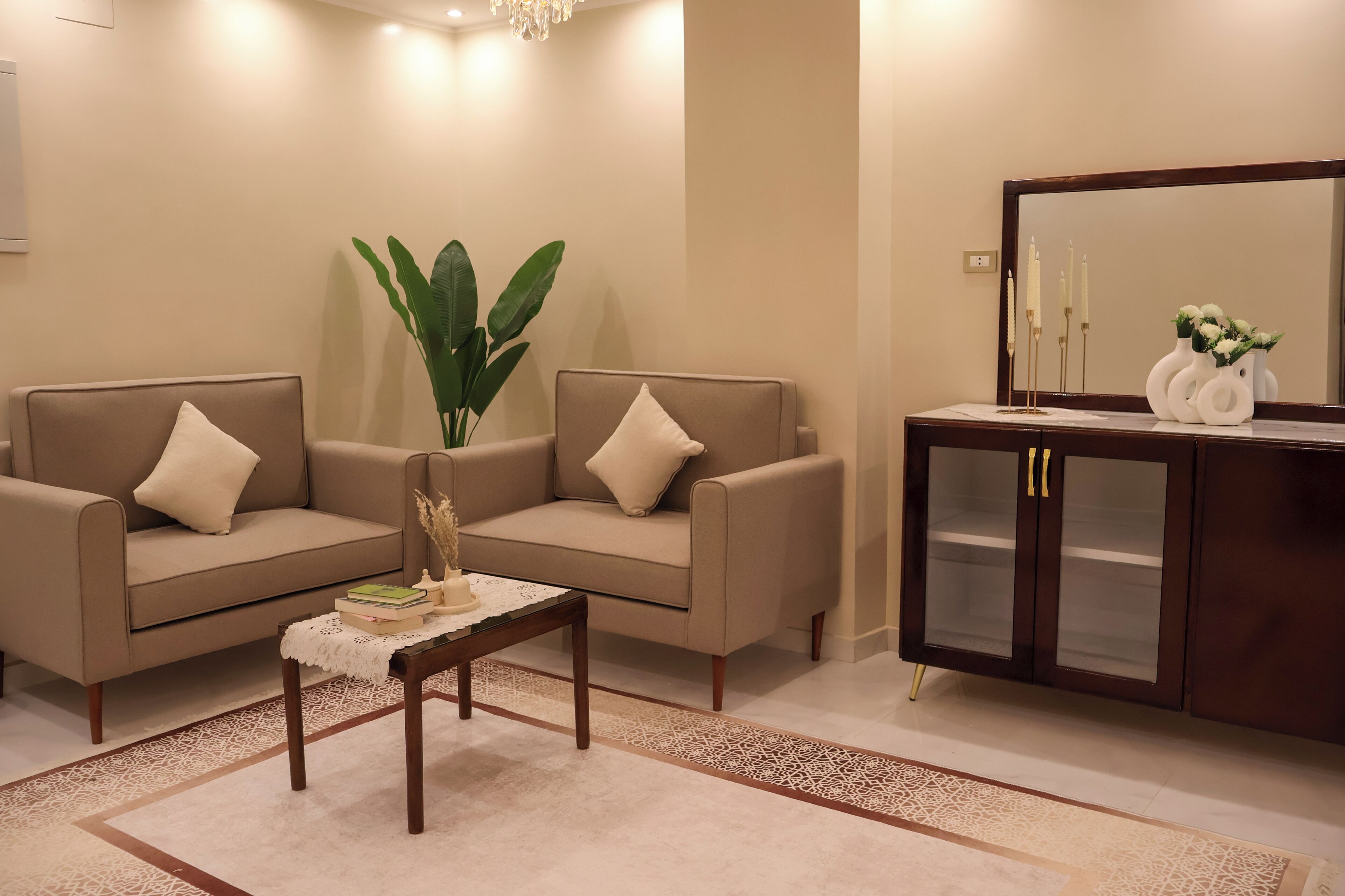 Ein Wohnzimmer mit zwei beigen Sofas, einem Couchtisch, einer großen Pflanze und einer Holzvitrine.