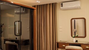 Habitación de hotel con cama, escritorio, silla, espejo y aire acondicionado.
