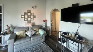 Un salon avec un canapé gris, un téléviseur à écran plat fixé au mur et une petite table sur laquelle se trouvent un vase et des bougies.