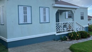 Une maison de plain-pied à la façade bleu clair, avec des volets blancs et un petit porche doté d’une balustrade.