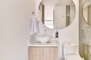 Een moderne badkamer met een ronde spiegel, een witte wastafel en een toilet.