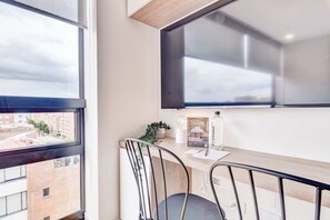 Een moderne kamer met een bureau, twee stoelen, een raam met uitzicht op gebouwen, en een wandtelevisie.