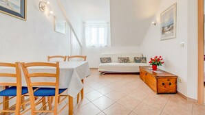 A dining area with wooden chairs and a table, a sofa with cushions, a wooden chest of drawers, and a potted plant. - 1 bedroom pet friendly apartment in Bol (Bol)