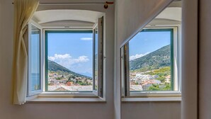 Una habitación con dos ventanas abiertas que dan a una villa en la ladera.