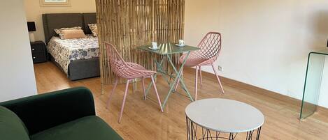 A modern room with a bed, a green sofa, a dining table with chairs, and a small round table.