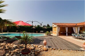 A pool area with lounge chairs, a red umbrella, and a dining area with outdoor seating. - Independent studio for 2 people with swimming pool. (Carpentras)