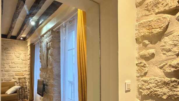 A room with a stone wall, a wooden ceiling, a sofa, a TV, and a door with curtains. - Paris Loft for 4 by Châtelet & Montorgueil & Metro (PARIS)