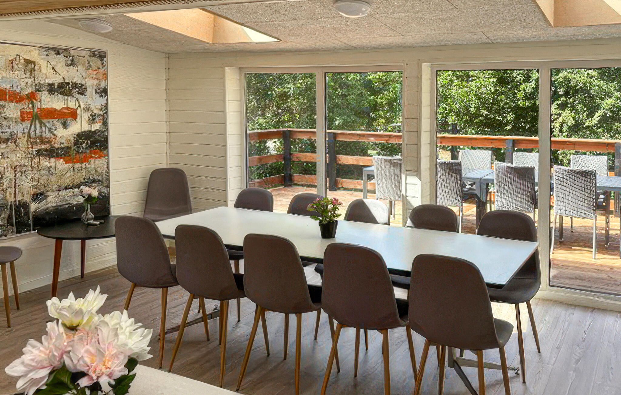 A dining area with a table and chairs, large windows, and a view of greenery outside.