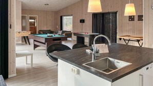 A modern kitchen with a built-in sink, wooden panel walls, and a pool table in the background. - Beautiful home in Hadsund with WiFi (Hadsund)