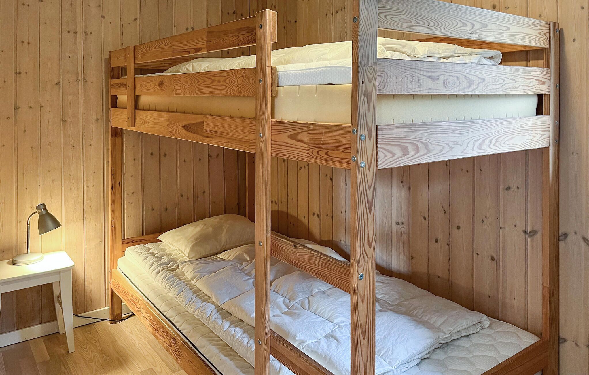 Ein Etagenbett mit zwei Schlafstellen, ein Nachttisch mit Lampe und Holzwände.