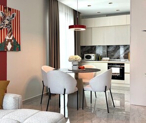 Eine moderne Küche mit Mikrowelle, Backofen und Marmor-Spritzschutz. Ein Essbereich mit zwei Stühlen und einem Tisch, darüber eine rote Pendelleuchte.