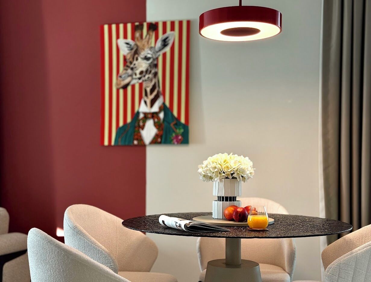 Una habitación de hotel moderna con una mesa redonda, un jarrón de flores y un cuadro de una jirafa en la pared.