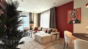 A modern living room with a sectional sofa, a dining area with a round table, and a large potted plant. - Apartment 2+1 Qoople Excellence B55 designer duplex by the sea (Alanya)