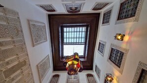 A room with intricate ceiling and wall designs, a large window at the center, and multiple wall-mounted light fixtures. - Riad Dar Salma  (Fes)