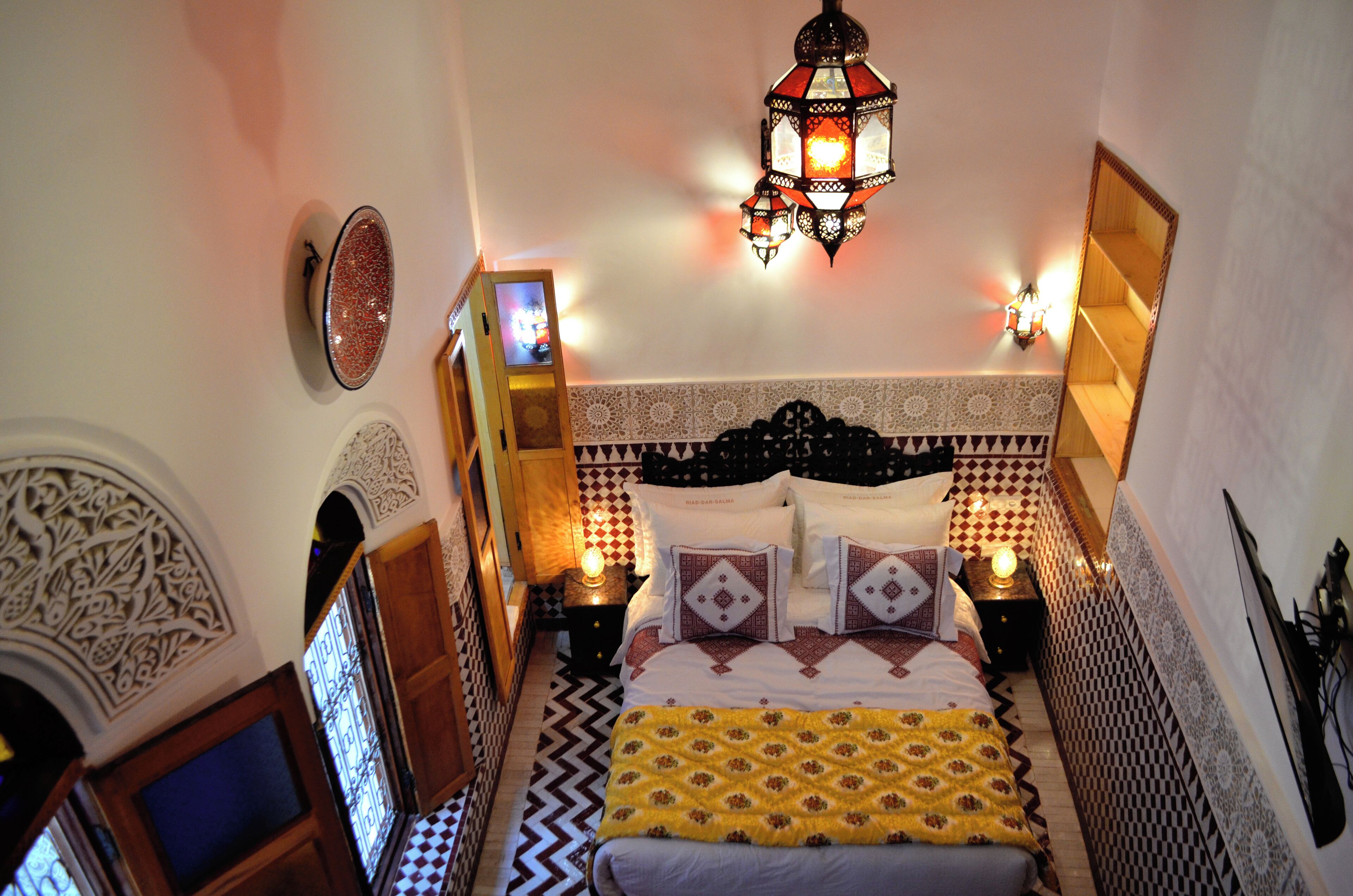 Ein Schlafzimmer mit einem gemusterten Kopfteil, einem Bett mit Kissen, einem Nachttisch mit Lampe und einem Wanddekor.