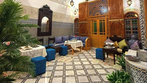 A traditional Moroccan interior with ornate tile work, a central seating area with sofas and a coffee table, and a hanging lantern. - Riad Dar Salma  (Fes)