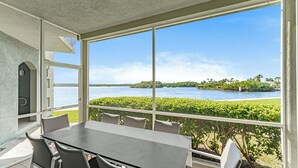 Ein Zimmer mit großem Fenster mit Blick auf ein Gewässer, einem Tisch mit Stühlen und einer kleinen, fest installierten Sitzgelegenheit.