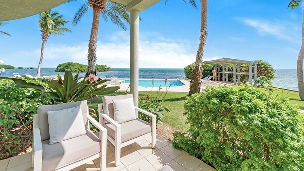 Ein überdachter Außenbereich mit Pool, Palmen und Blick aufs Meer.