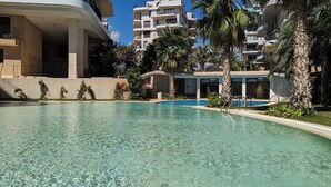 A swimming pool with clear water, surrounded by palm trees and modern buildings. - Allonbay Apartments (Villajoyosa)