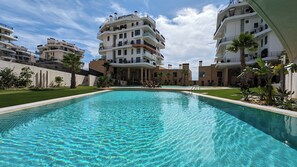 A swimming pool surrounded by modern multi-story buildings with balconies and a clear sky. - Aster Apartments (Villajoyosa)