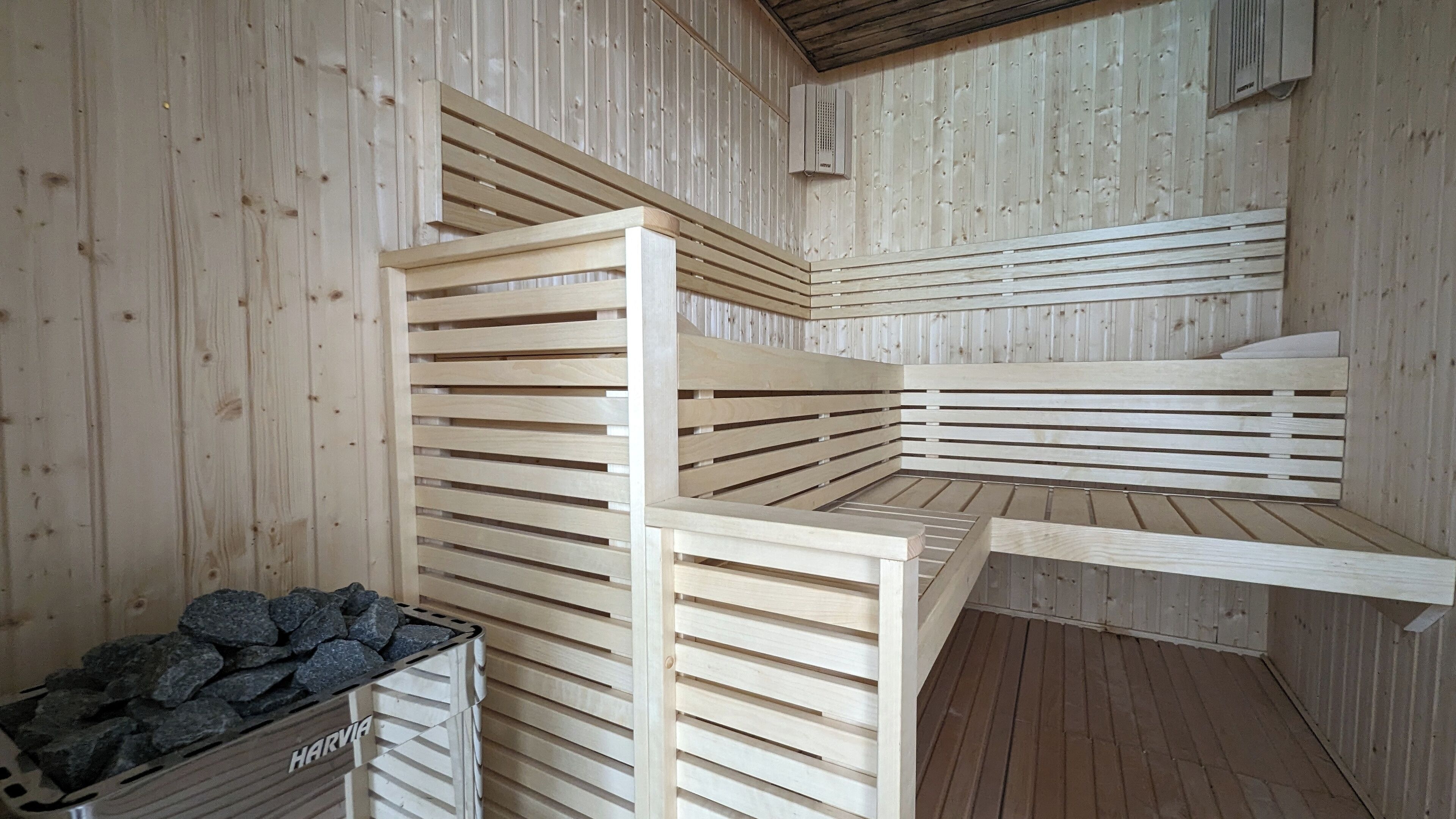 A sauna room with wooden benches and a stone-filled container labeled "HARVIA".